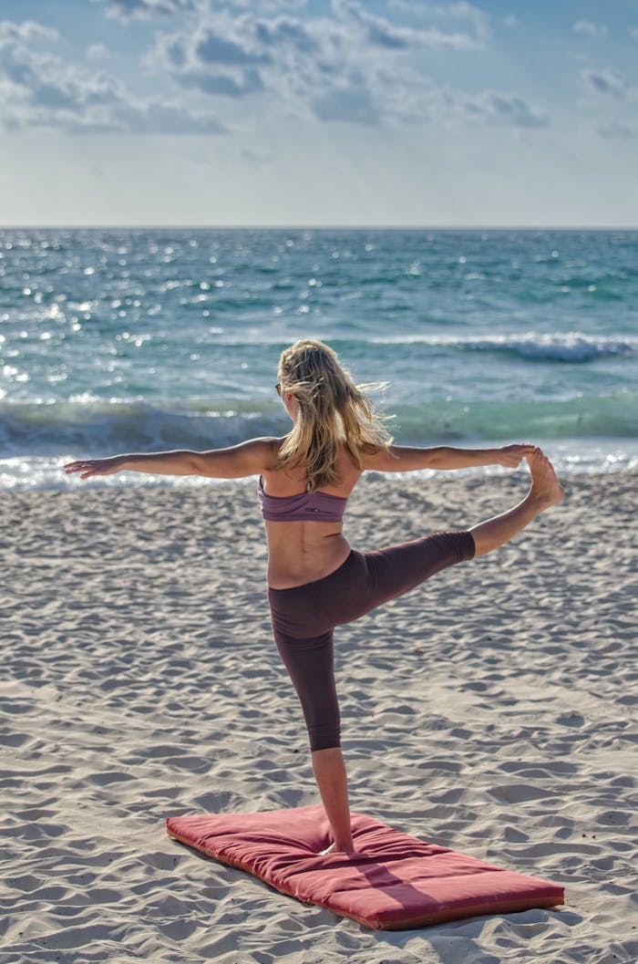 gallery-03 A woman performs yoga on a sandy beach at sunrise, embracing wellness and tranquility.