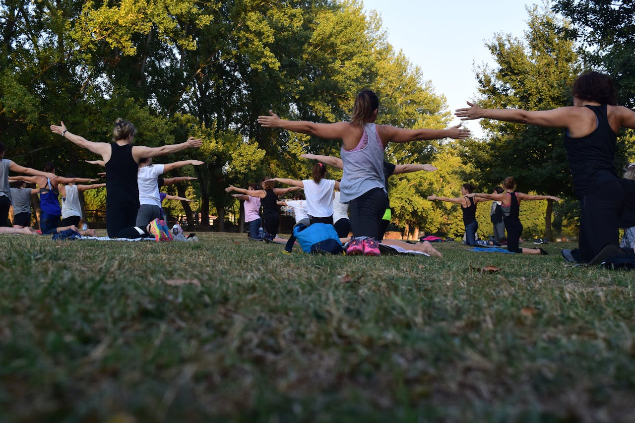 gallery-02 Group of adults practicing yoga outdoors in a park surrounded by trees.